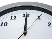 Close up of the top of an analogue clock, showing time as five seconds past twelve.